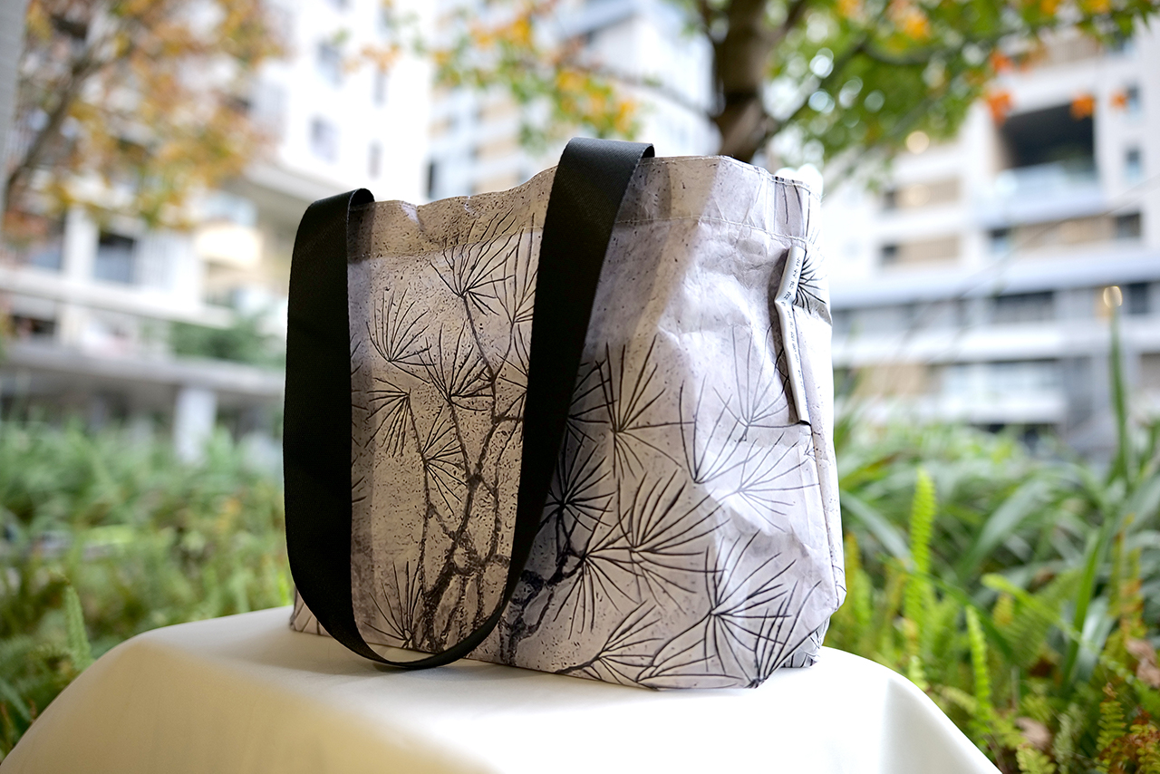 環保提袋／本項目結合永久性作品《採光》，選取作品局部的植物光影輪廓浮雕，印製於強韌耐磨、可重複利用和分解的杜邦泰維克材質，讓雋永的作品形象滲入日常生活使用，同時也兼顧永續環境理念。